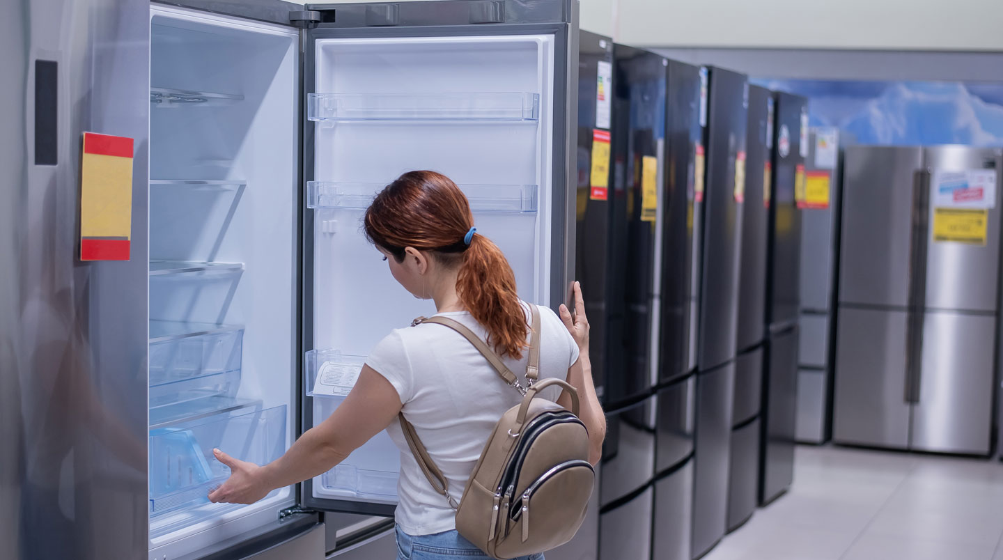 Vue en perspective d'une allée spacieuse de magasin d'électroménager avec appareils neufs exposés sur des présentoirs blancs sous éclairage LED
